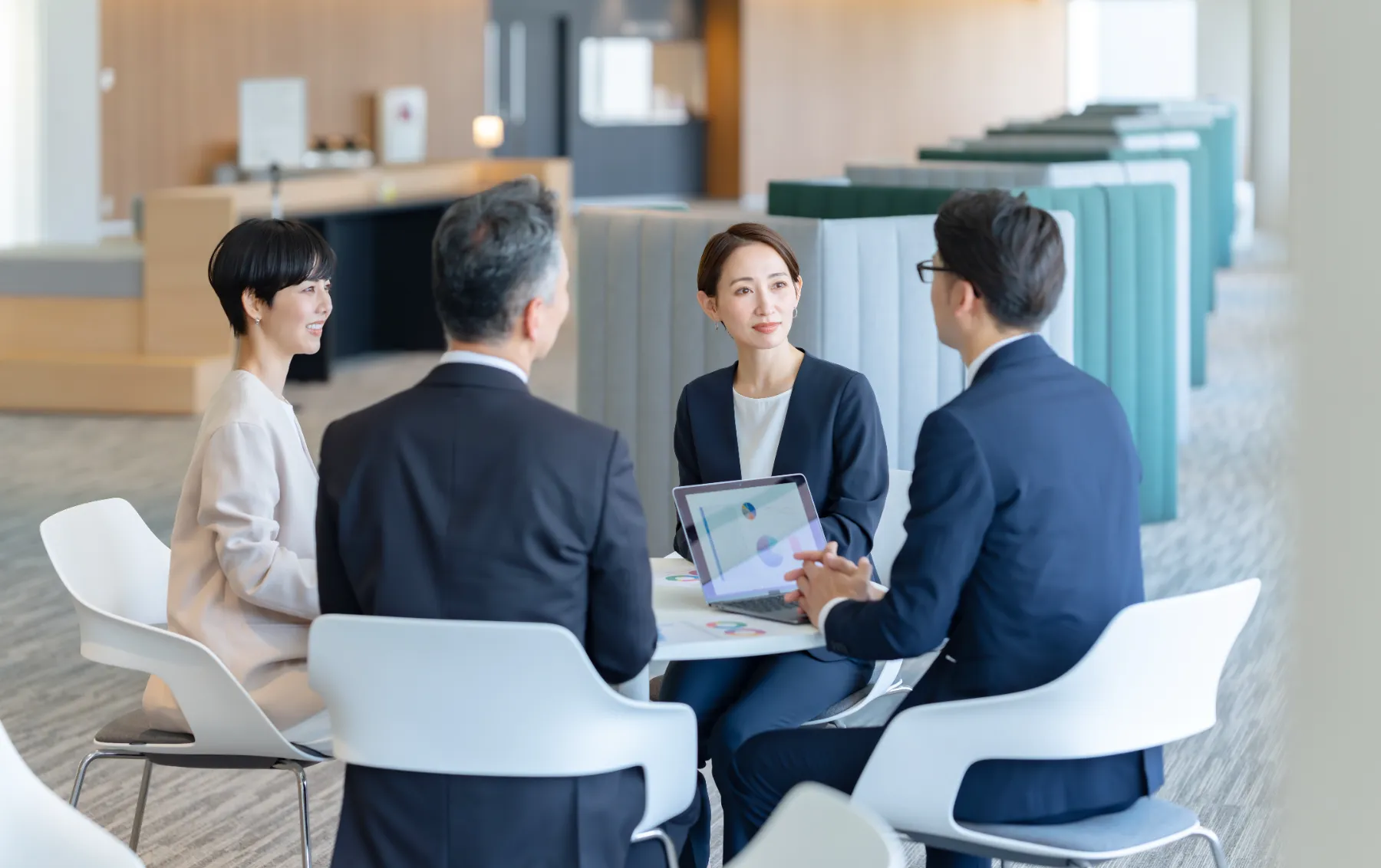 明るいオフィスラウンジで資料を手に打ち合わせをする4人のビジネスパーソン